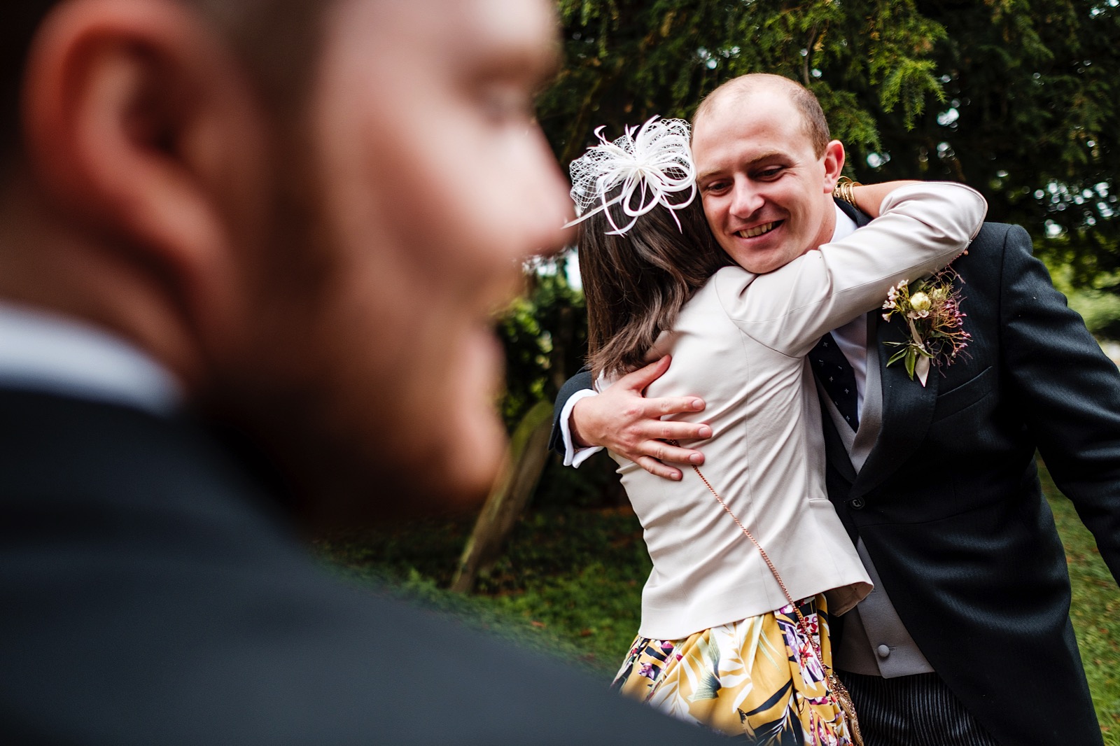Street Photography influenced photograph of a guest hugging another guest, using the side of an ushers face to frame the moment